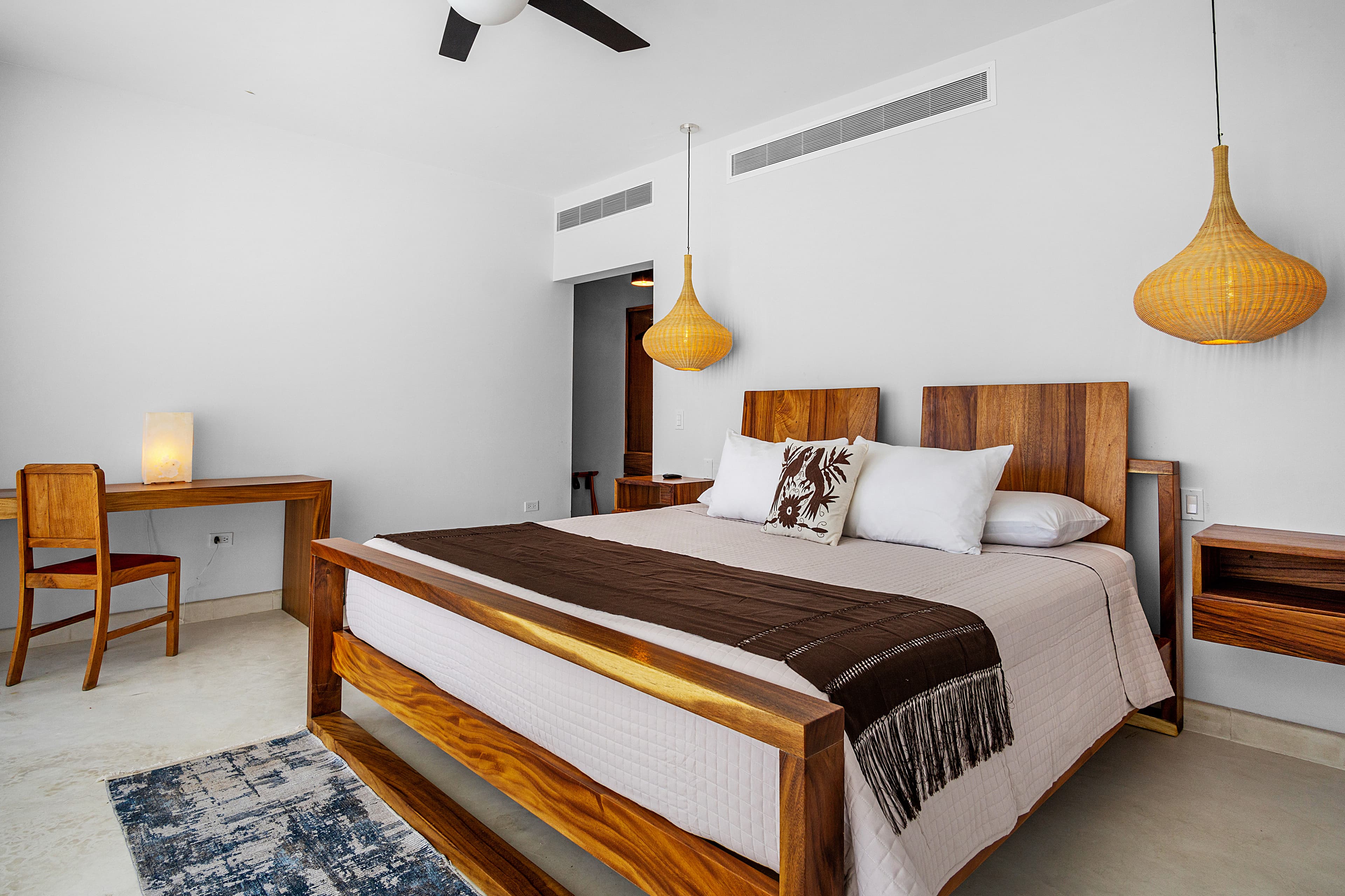 A modern bedroom featuring a wooden bed, pendant lights, and a minimalist aesthetic.
