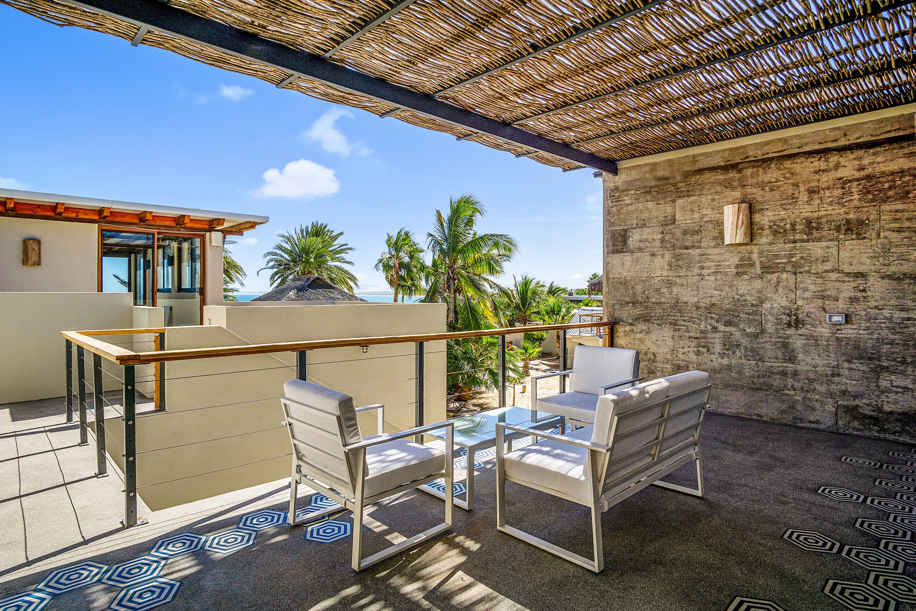 A serene balcony with two white chairs overlooking palm trees and a blue sky.