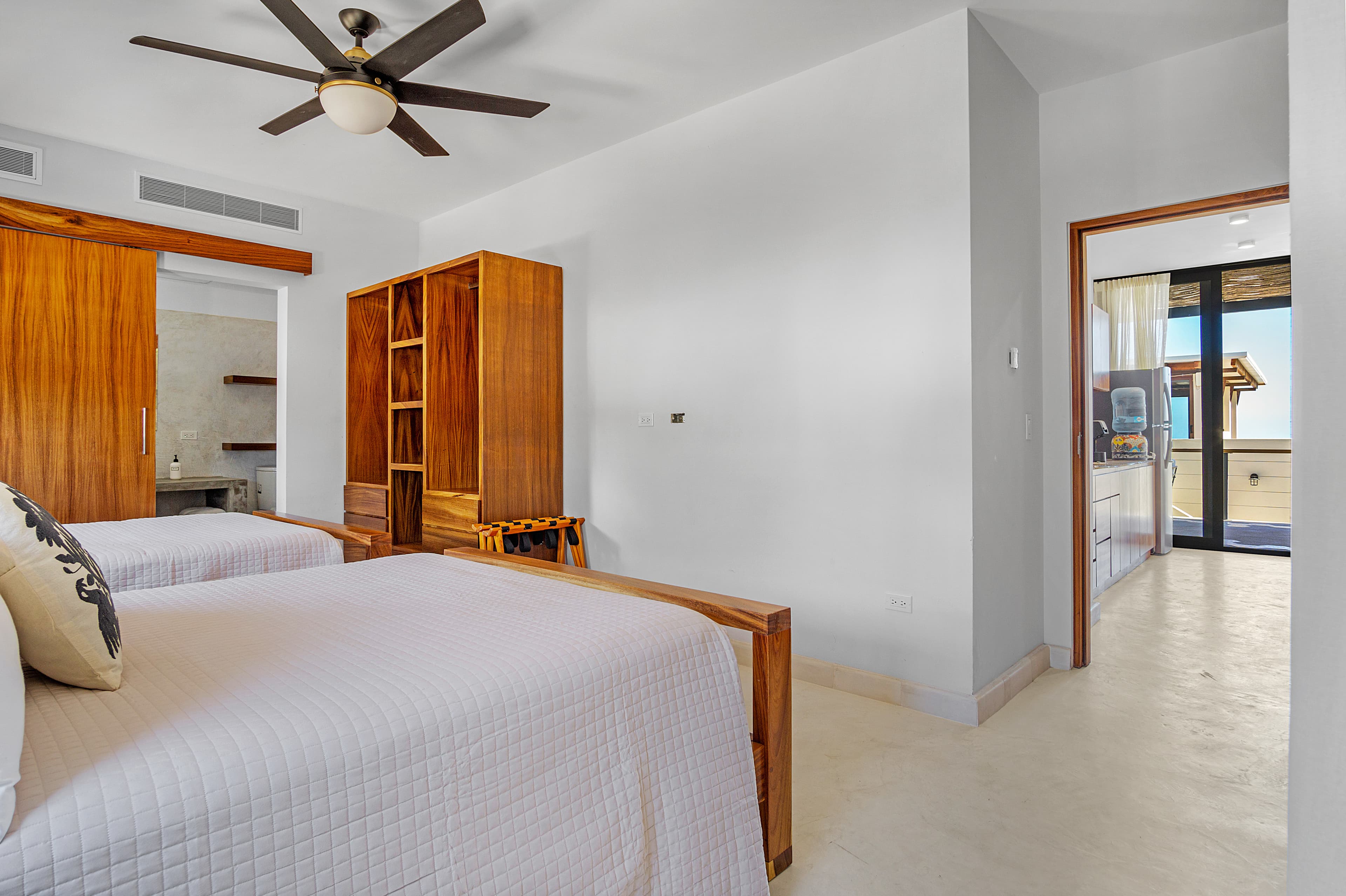 A modern bedroom featuring two wooden beds, a ceiling fan, and a doorway leading to an exterior space.