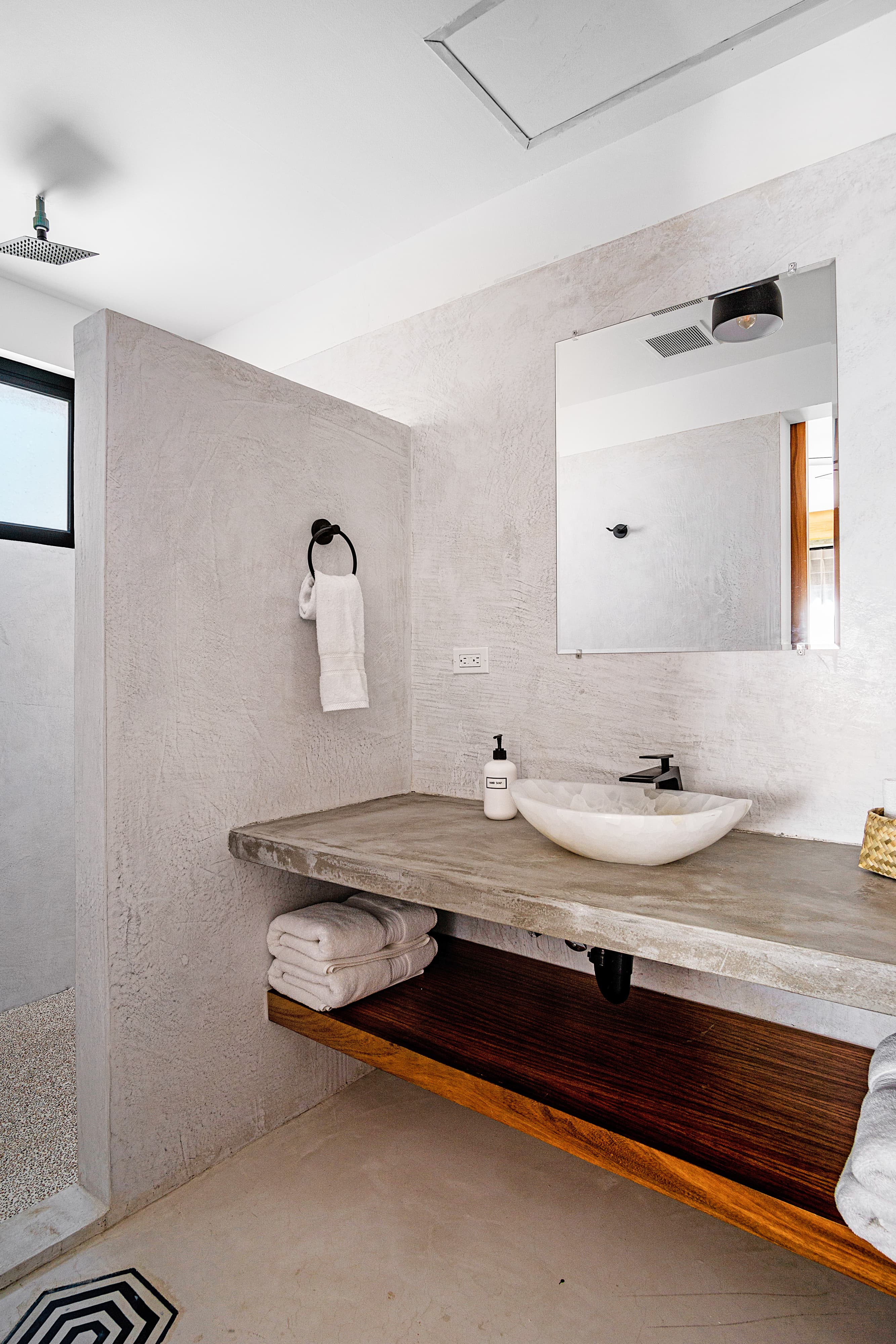 Modern bathroom with a concrete sink, wooden shelving, and a large mirror.