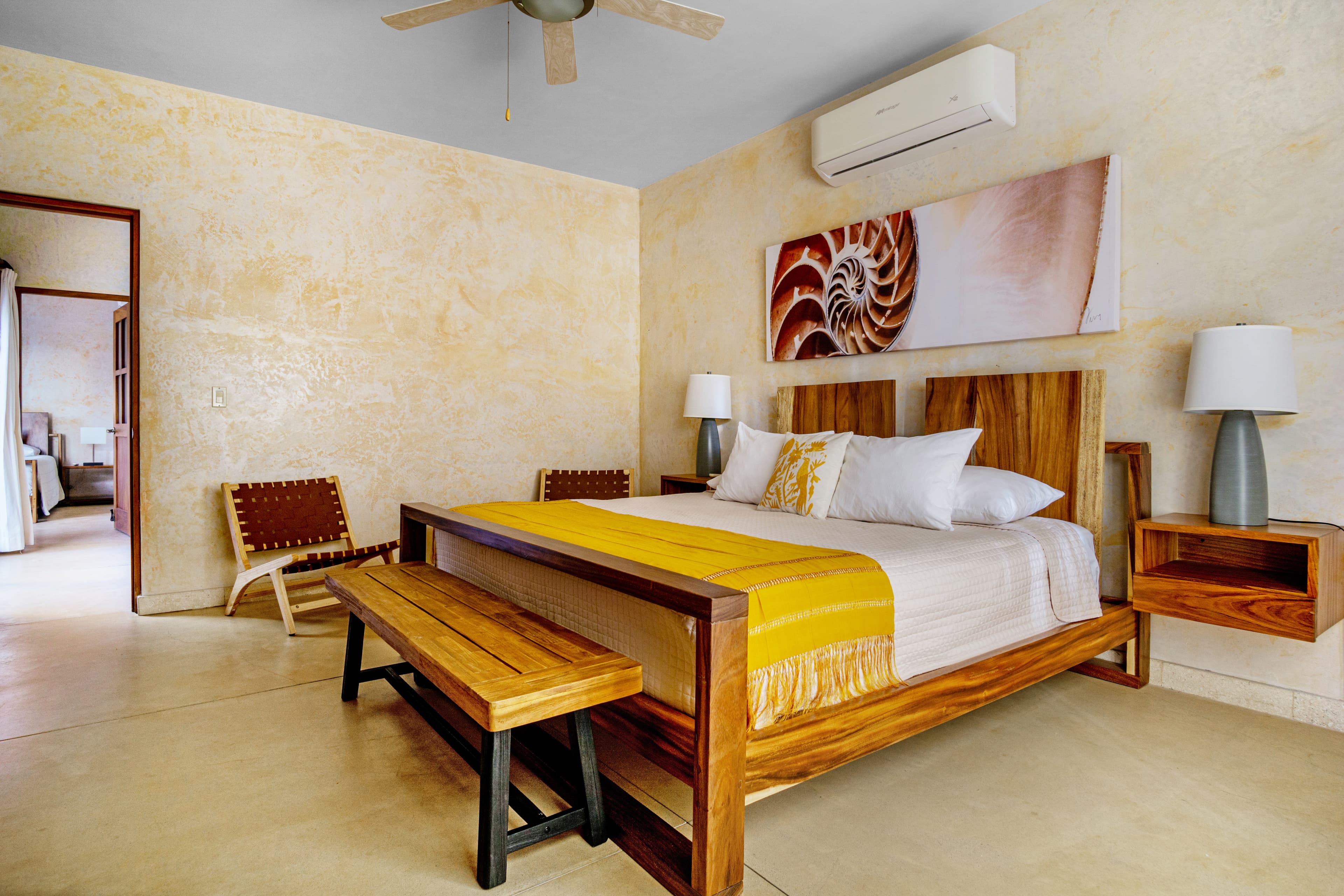 A cozy bedroom featuring a wooden bed, a yellow accent blanket, bedside lamps, and minimalist decor.