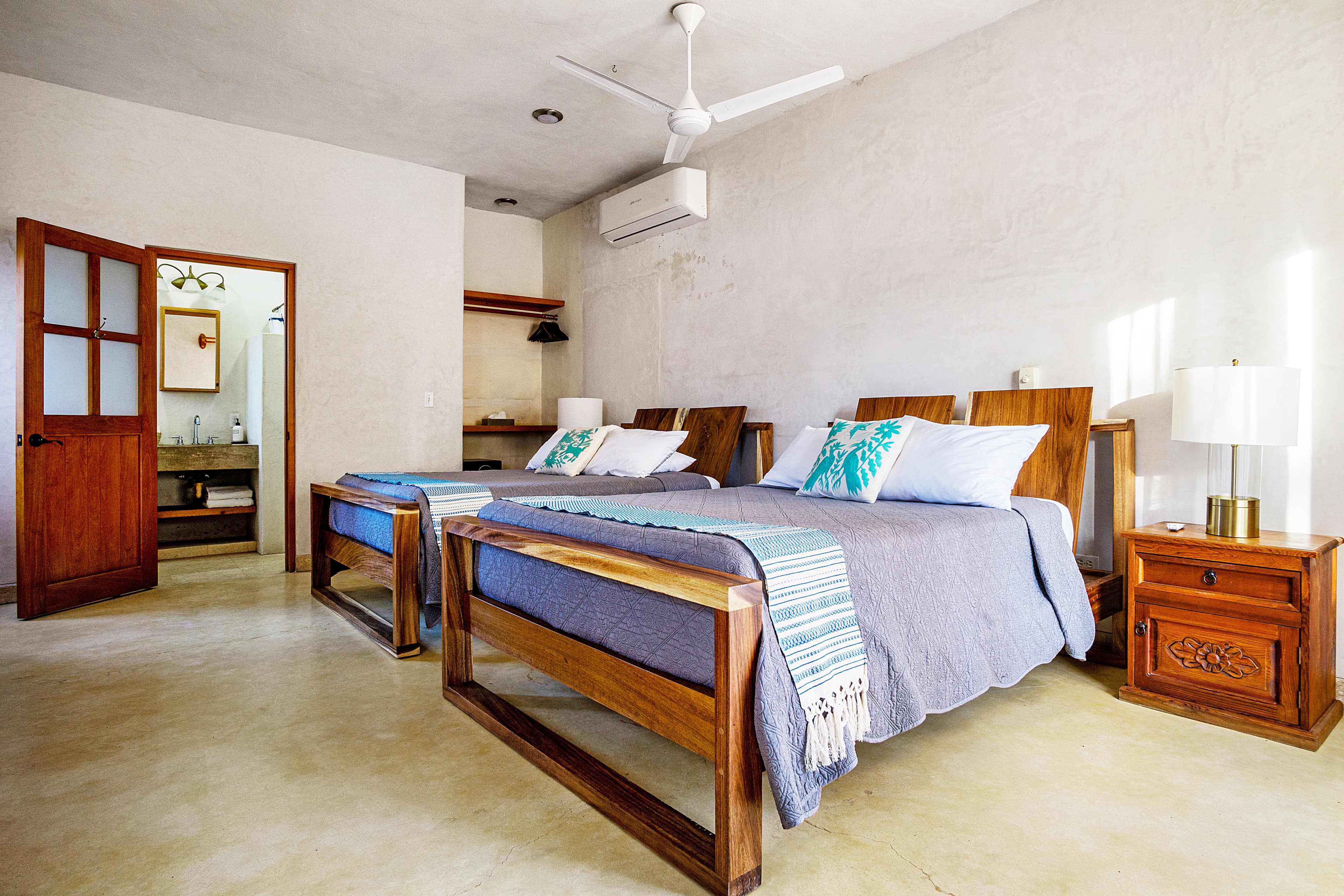 Cozy bedroom featuring two wooden beds, decorative pillows, a ceiling fan, and an adjoining bathroom.